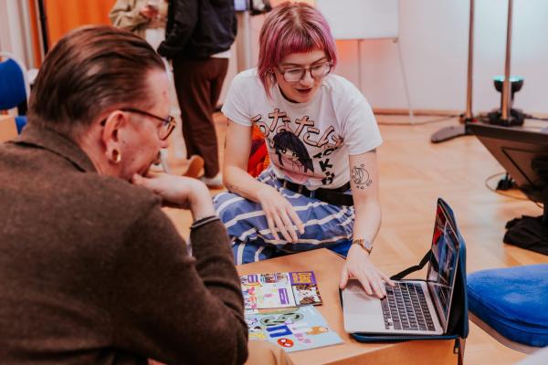 Vrouw met bril en roze haar wijst iets aan op laptop