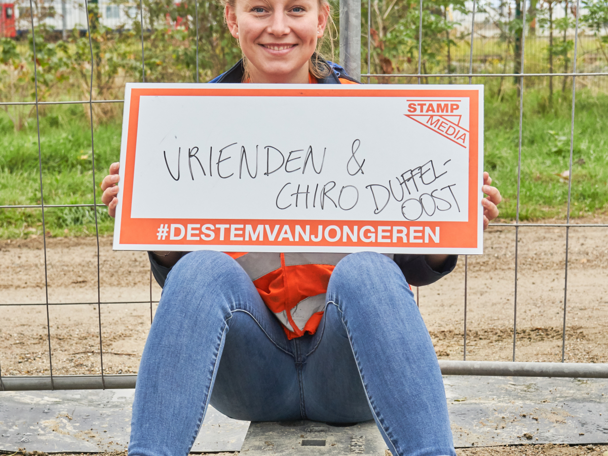 Jongere met bordje vast met 'vrienden en chiro Duffel-Oost' op