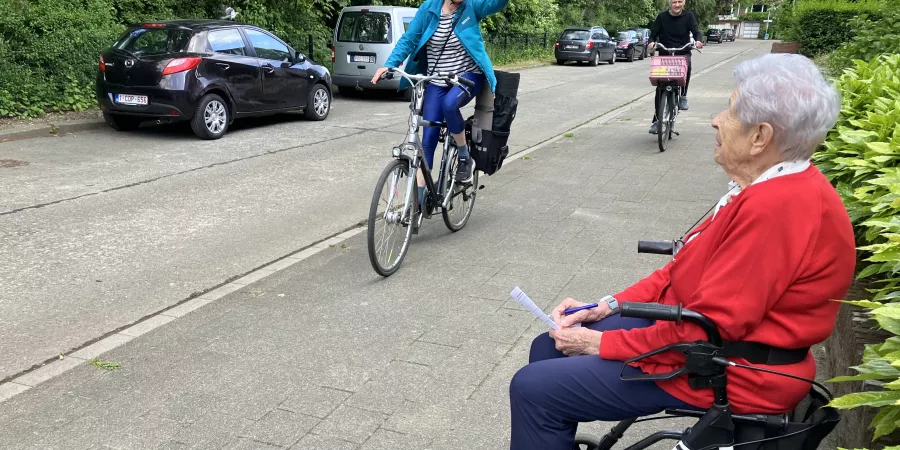 Een vrouw zittend op een rollator telt het verkeer op straat