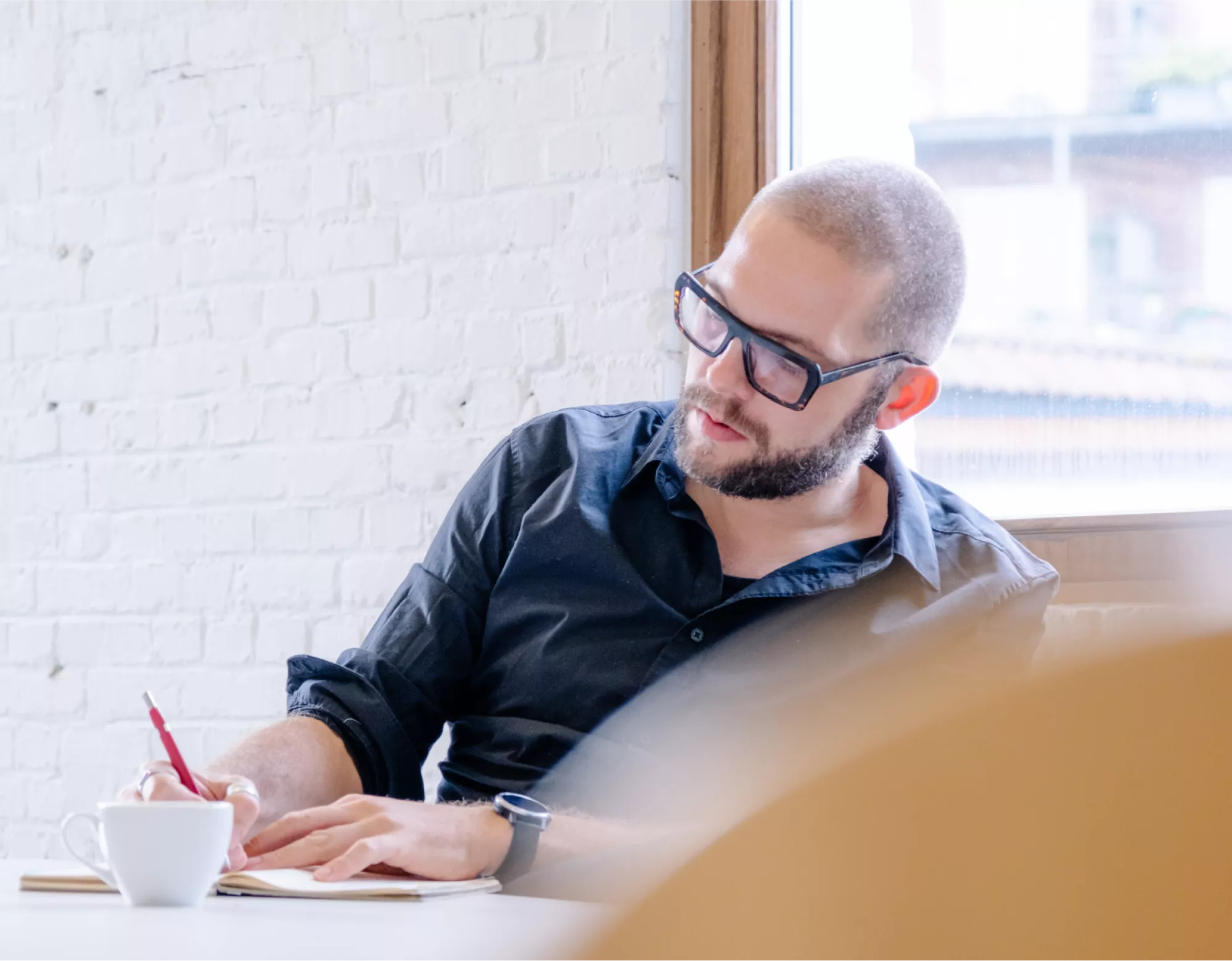 Een copywriter in een hemd is aan het schrijven in zijn notitieboek in een goed verlichte office ruimte