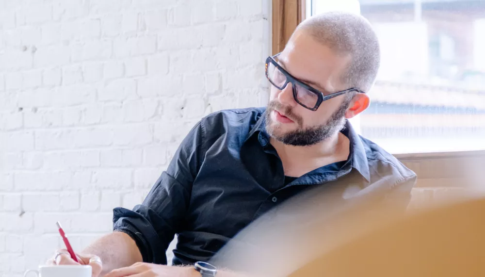 Michiel aan het werk Een copywriter in een hemd is aan het schrijven in zijn notitieboek in een goed verlichte office ruimte